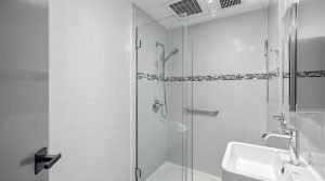 A compact, modern bathroom in New Westminster, BC, featuring a glass-enclosed walk-in shower with a handheld showerhead, a small vanity, and sleek chrome fixtures.